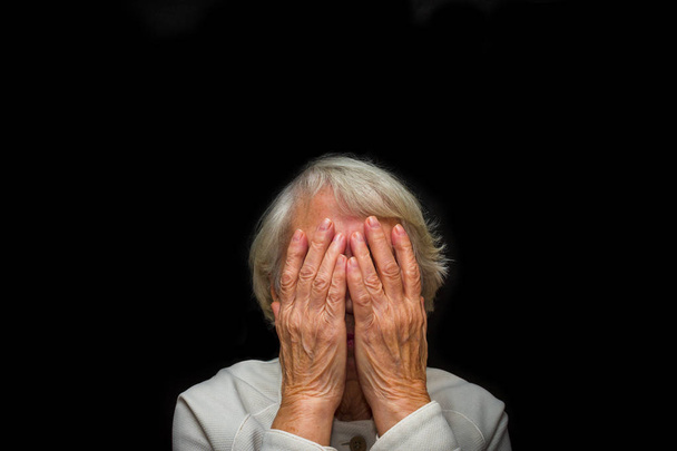 Portret van een oudere vrouw met gezicht gesloten door handen - Foto, afbeelding
