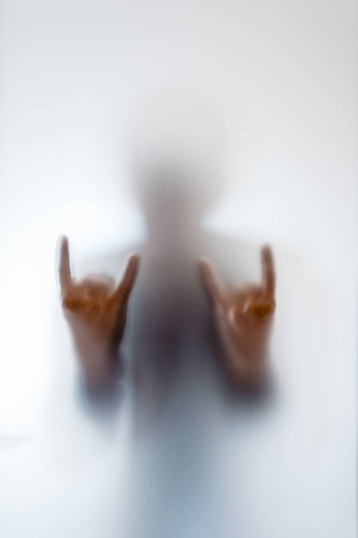 Man doing a rock gesture behind a frosted glass - Фото, изображение