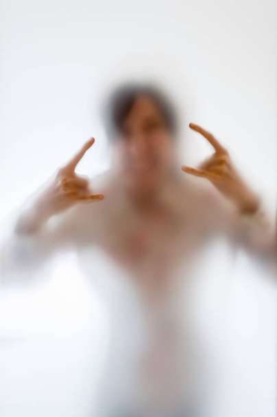 Mulher fazendo um gesto de rocha atrás de um vidro fosco
 - Foto, Imagem
