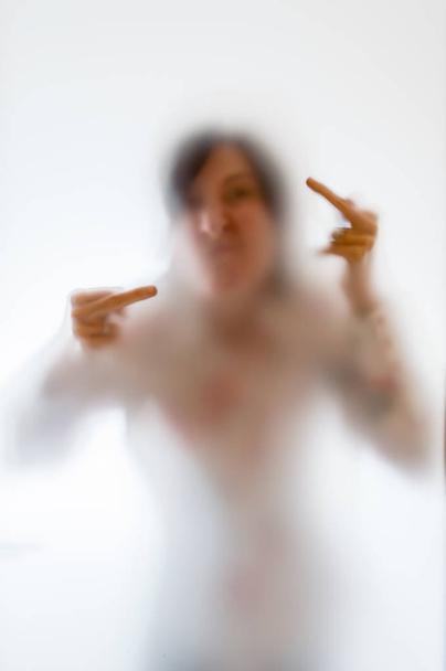 Θολή εικόνα μιας γυναίκας δείχνει το μεσαίο δάκτυλο πίσω από froste - Φωτογραφία, εικόνα