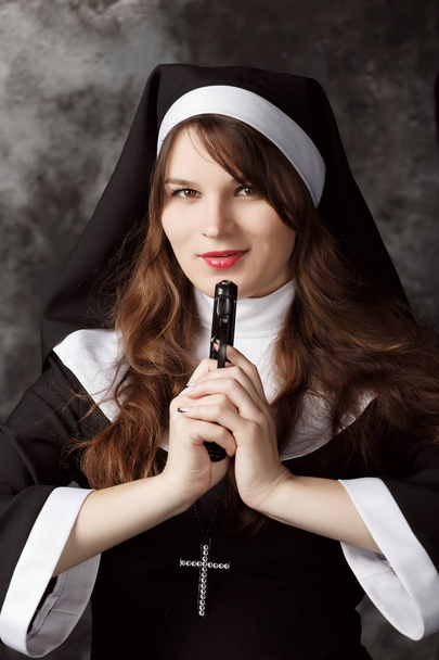attraktive Nonne mit Pistole in der Hand auf dunklem Hintergrund - Foto, Bild
