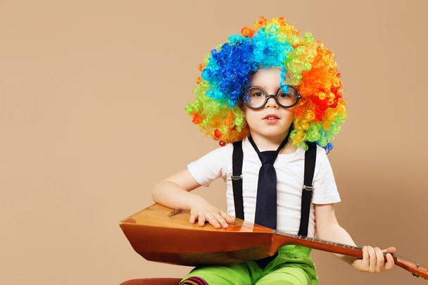 Blitheome enfants. Joyeux garçon clown en grande perruque néon jouant de la balalaika. Portrait d'enfant portant une perruque de clown et des lunettes
 - Photo, image