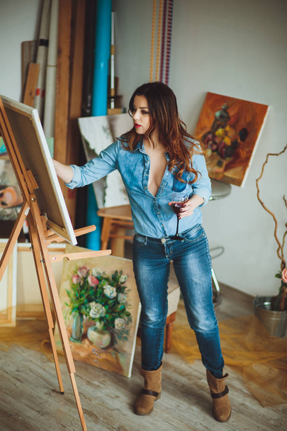 Woman artist painting a picture in a studio. Creative pensive painter girl paints a colorful picture on canvas with oil colors in workshop. - Photo, Image
