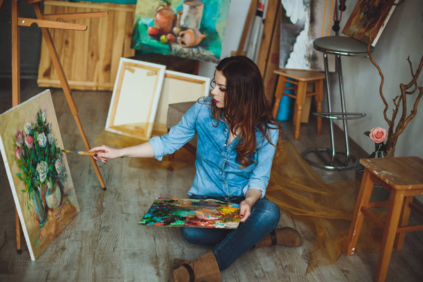 Nő művész festeni egy képet a stúdióban. Kreatív töprengő festő lány fest egy színes képet műhely színeivel olaj vászon. - Fotó, kép