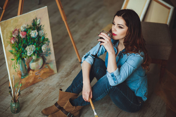 Woman artist painting a picture in a studio. Creative pensive painter girl paints a colorful picture on canvas with oil colors in workshop. - Fotoğraf, Görsel