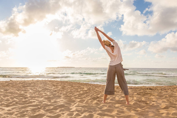 Woman practicing yoga on sea beach at sunset. - Fotografie, Obrázek