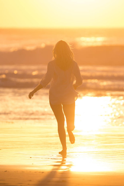 Γυναίκα που τρέχει στην παραλία στο ηλιοβασίλεμα. - Φωτογραφία, εικόνα