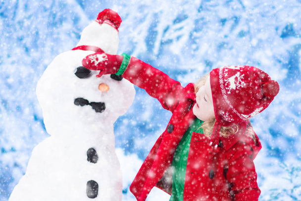 Маленькая девочка строит снеговика зимой
 - Фото, изображение