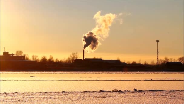 inquinamento ambientale con gas nocivi. fumo dal camino viene rilasciato in aria sullo sfondo del sole al tramonto accanto al fiume. un problema ambientale. inverno. - Filmati, video