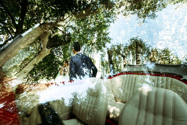 Bride with a bouquet and a groom behind a car - Φωτογραφία, εικόνα