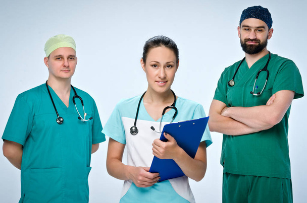 A team of three young doctors. The team included a doctor and a woman, two men doctors. They are dressed in scrubs. On the necks of doctors hang pediatric phonendoscopes. - Фото, изображение
