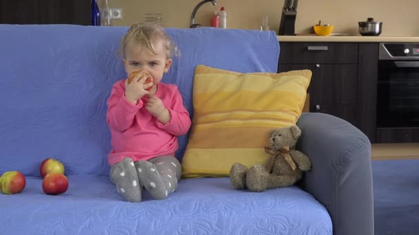 Gorgeous toddler kid child sitting on the sofa and eating big apple fruit. - Video