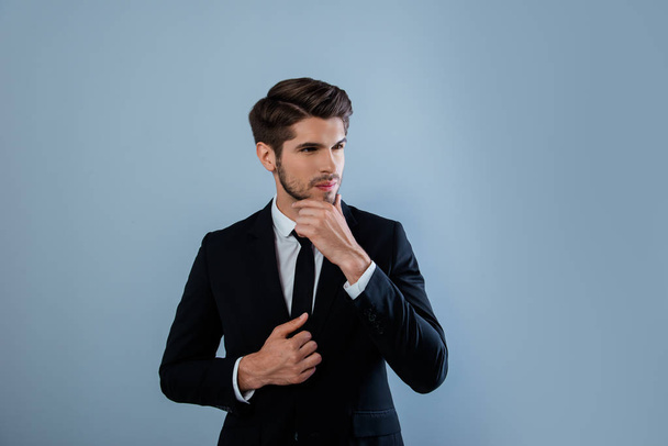 Minded young businessman in black suit touching his face - Φωτογραφία, εικόνα