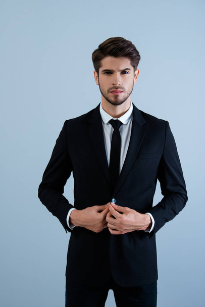 Serious young businessman buttoning his suit on gray background - Fotoğraf, Görsel