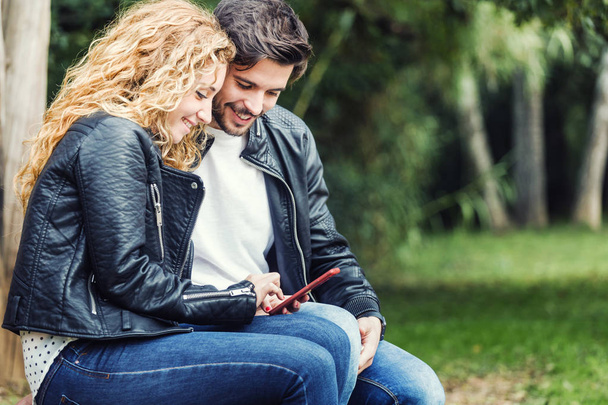 Beautiful young couple using they mobile phone in the park. - Photo, image