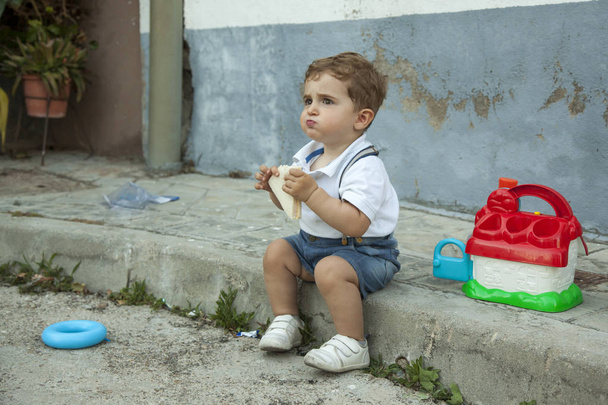 Full shot portrait cute baby boy having a snack sit in the sidew - Zdjęcie, obraz