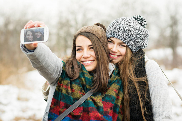 Two teenage girls taking a selfie in winter - Foto, afbeelding