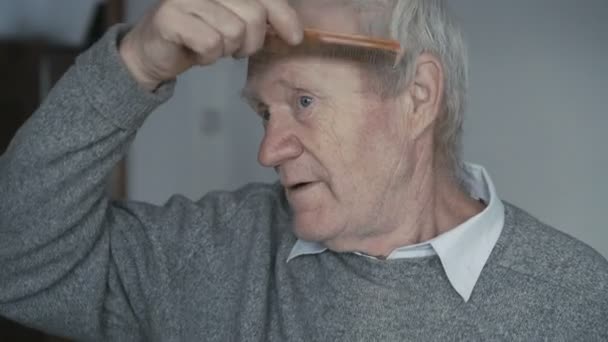 The senior is combing his short hair with a wooden comb 4K - Video, Çekim