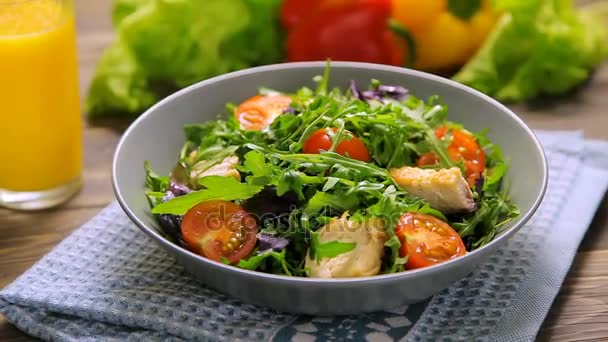 Frisse salade met kip, tomaten, rucola, mesclun, basilicum en sinaasappelsap op een doek servet, op houten tafel - Video