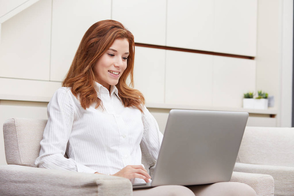  Smiling happy woman sitting on the sofa and using laptop - 写真・画像