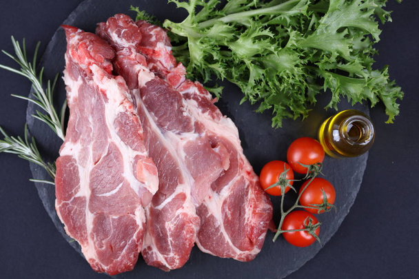 Raw pork neck meat on black background, spices, vegetables, olive oil. Cooking background, healthy eating concept. - Photo, Image