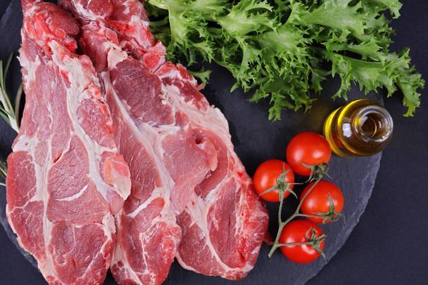 Raw pork neck meat on black background, spices, vegetables, olive oil. Cooking background, healthy eating concept. - Photo, Image