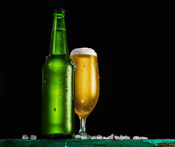 Bottle and glass of beer on the wooden table over black background. - 写真・画像