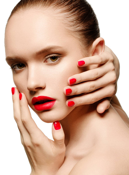 Молодая женщина с красными губами и красными ногтями, прикасаясь к лицу
 - Фото, изображение
