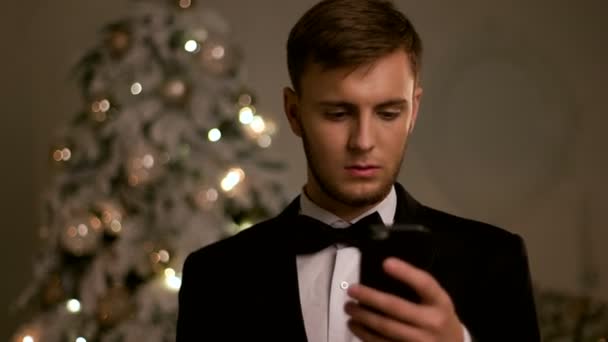 Mladý pohledný muž v stylovém obleku, chatování na mobilním telefonu na nový rok den. - Záběry, video