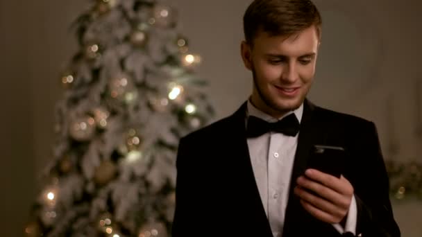 Молодой красивый мужчина в стильном костюме, болтает по мобильному телефону в новогодний день
. - Кадры, видео