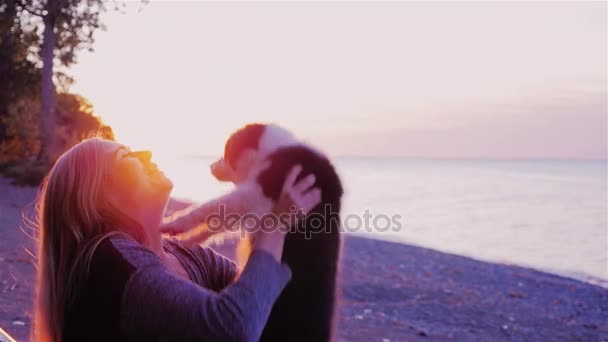 Játszani a kedvenc kutya. Nő a kiskutya dob felső, játszik vele. A tenger vagy tó naplemente háttér - Felvétel, videó