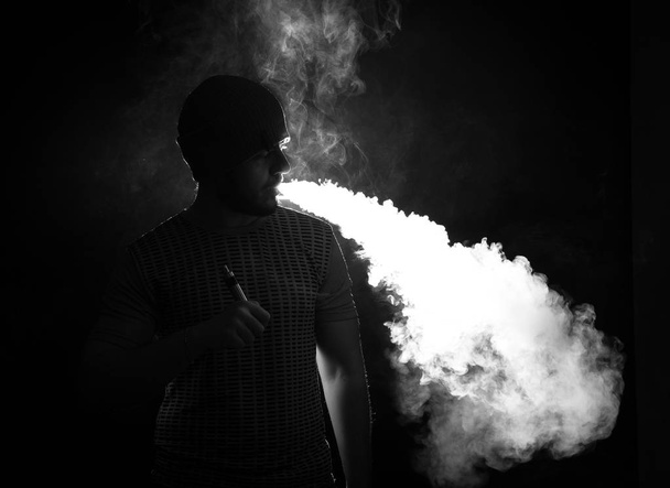 Men with beard vaping on black background in hat - Foto, immagini