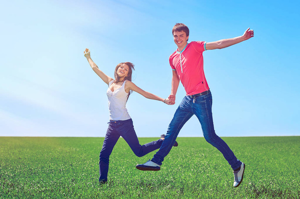Happy couple jumping in green field - Фото, изображение