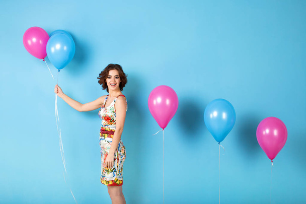 Young cheerful woman with helium balloons on a blue background. - Foto, afbeelding