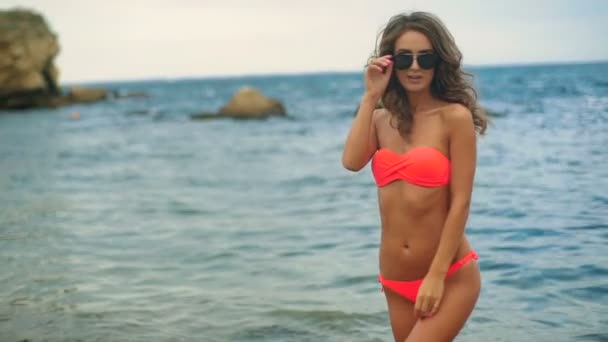 Aantrekkelijke jonge model dragen zwemmen pak en zonnebril poseren op de camera in een strand. - Video