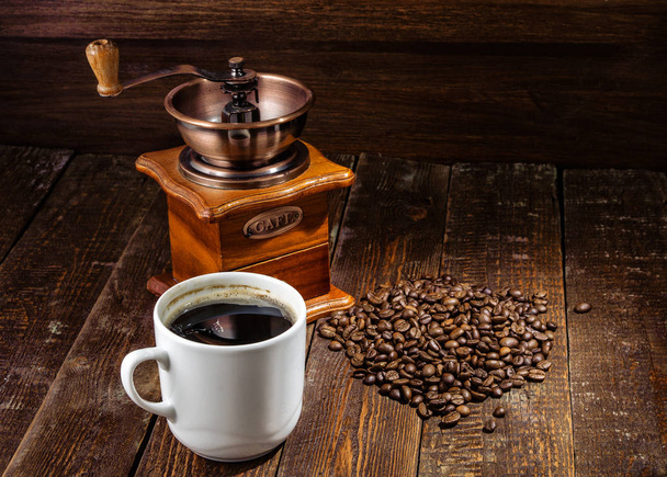 Taza de café de primer plano con molino de café sobre fondo de madera oscura
 - Foto, Imagen