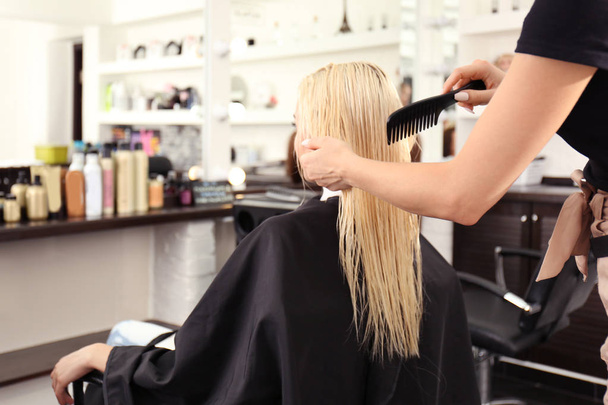 Hairdresser combing blonde's hair at salon - Foto, Imagem