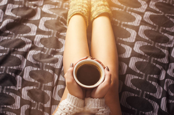      Detalhe da jovem mulher sexy e luz do sol. Mulher manter uma xícara de café e ler um livro. Ela está sentada em um cobertor.. pernas nuas. Ambiente doméstico
.  - Foto, Imagem