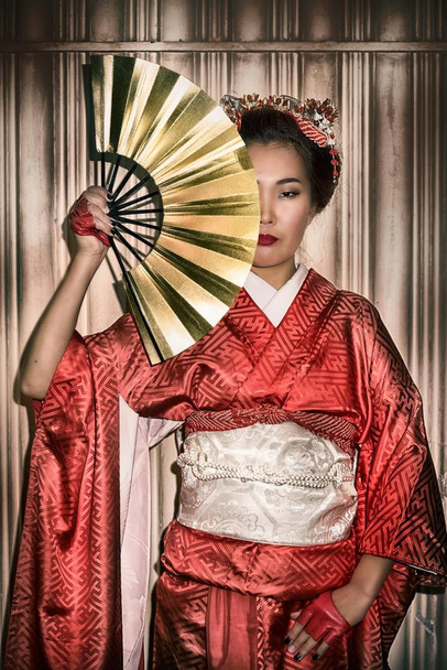 Femme asiatique en Kimono rouge traditionnel tenant un ventilateur en papier, qui couvre la moitié de son visage
. - Photo, image