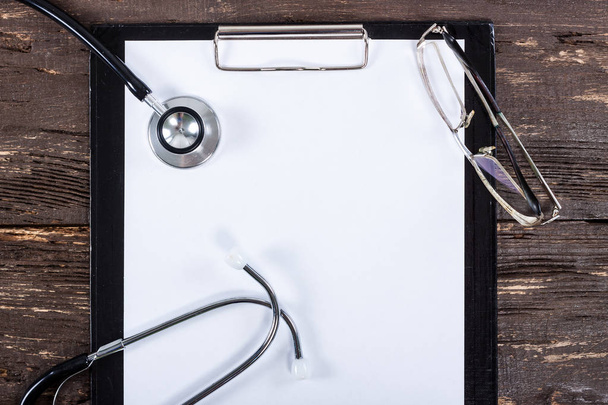 Medical clipboard and stethoscope on dark wooden table. - Photo, Image