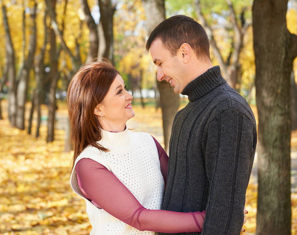 happy adult couple embrace in autumn city park, trees with yellow leaves, bright sun and happy emotions, tenderness and feelings - Valokuva, kuva