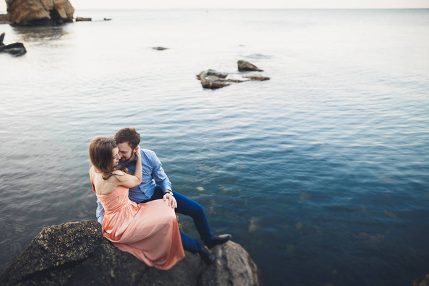 Wedding couple sitting on large stone around blue sea - Фото, зображення
