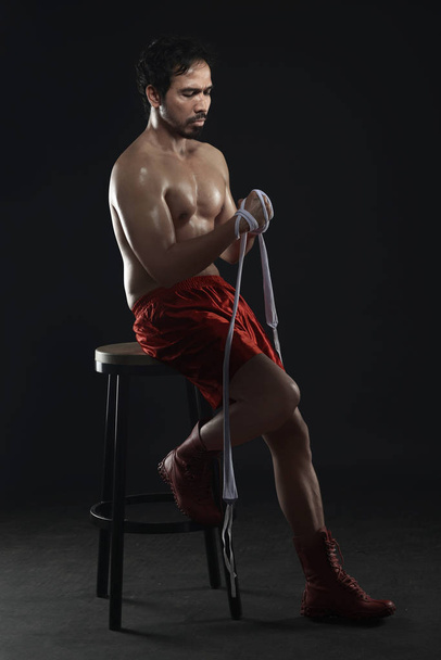 Sporcu adam Asya boksör beyaz askıları giyerken sandalyede oturan - Fotoğraf, Görsel