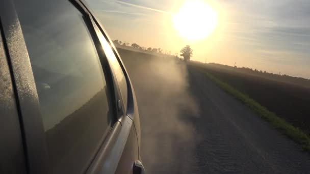 Stof stijgt van auto wielen auto rijden op landelijke grind weg avondzon in hemel. 4k - Video