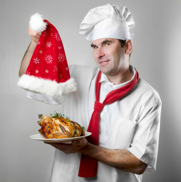 Chef showing plate with chicken and Santa hat - Photo, image
