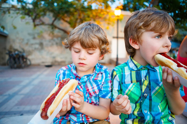 Два маленьких мальчика едят хот-доги на улице
 - Фото, изображение