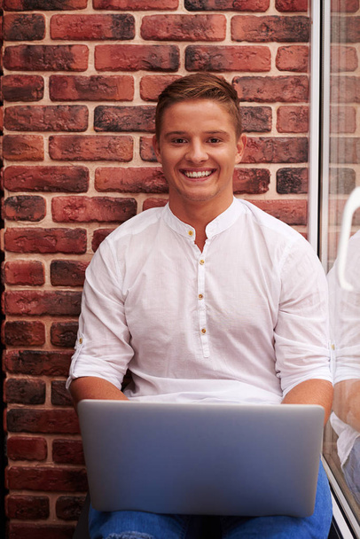 Relaxed young man using laptop sitting on windowsill over red br - Photo, image