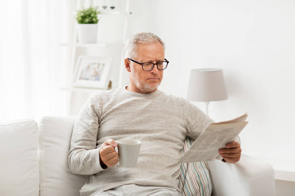 senior man in glasses reading newspaper at home - Fotó, kép