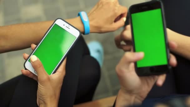 Δύο αθλητριών συνεδρίαση σε έναν πάγκο, κρατώντας δύο smartphone στα χέρια. Πράσινη οθόνη Chroma Key. Κοντινό πλάνο. - Πλάνα, βίντεο