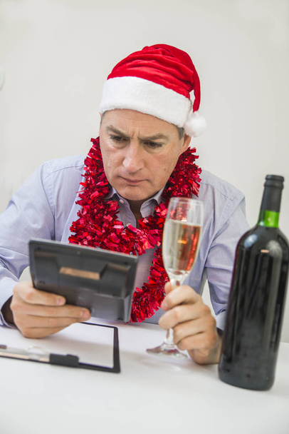 Photo Of Young Depressed Businessman Sitting In Office. Business Man Celebrate Merry Christmas And Happy New Year Wear Santa Hat - Foto, Imagen